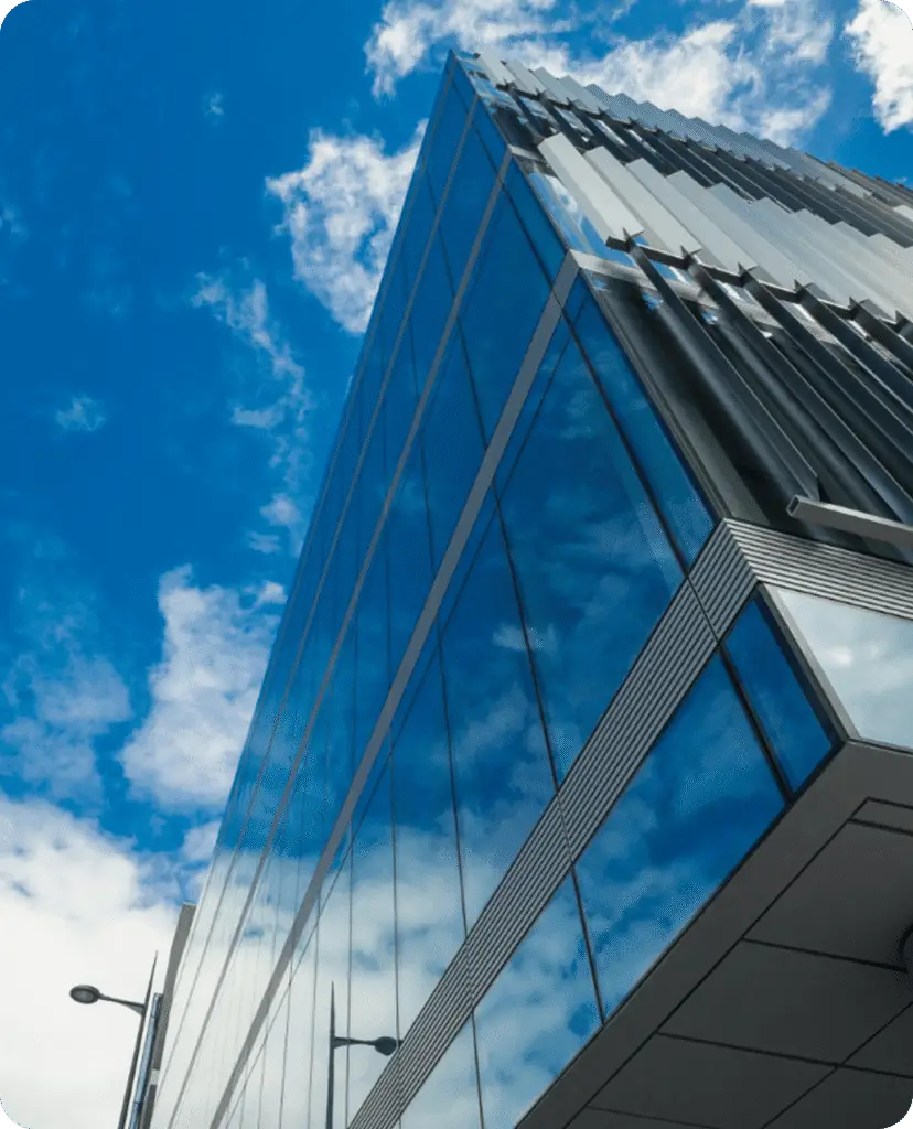 Modern glass-clad office building photographed from below against a blue sky